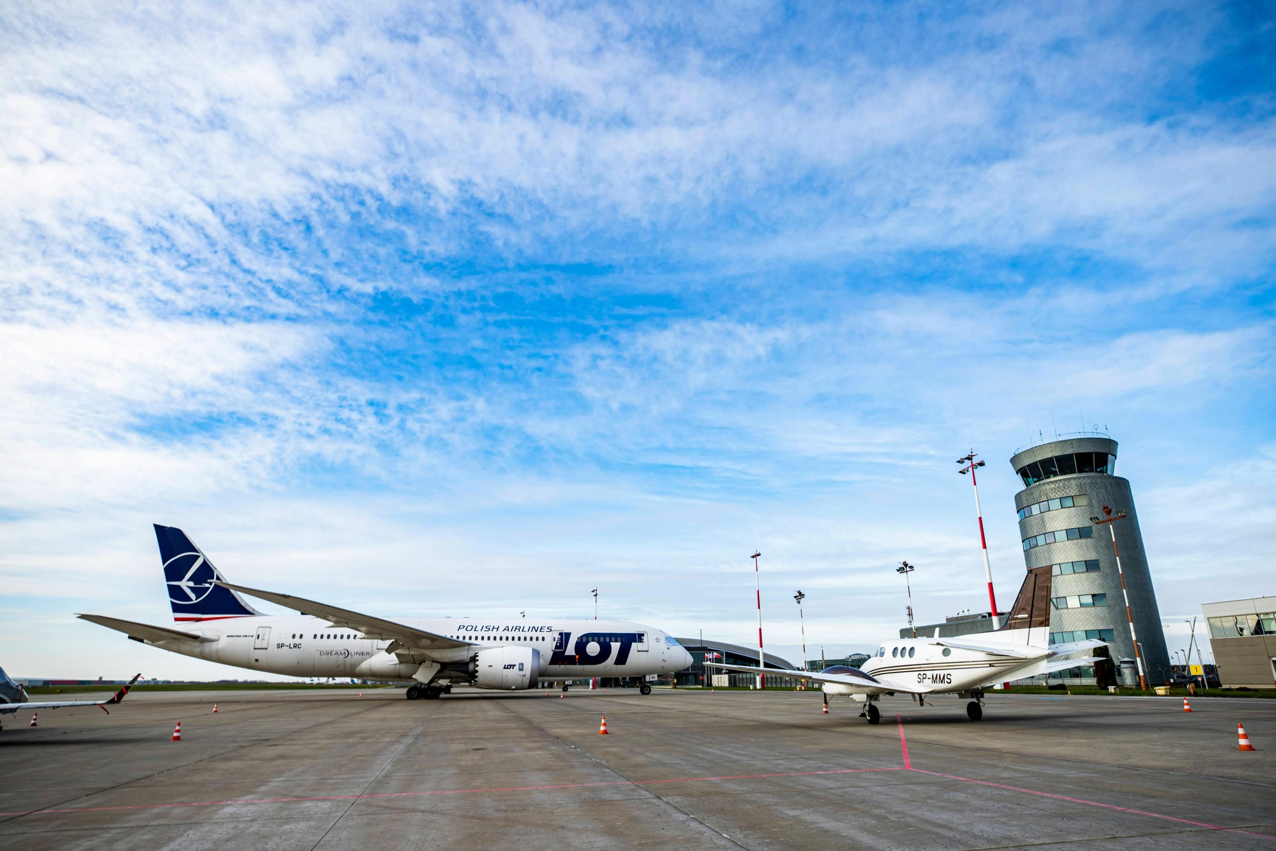 Polish Airlines plane on runway with control tower and jet under a blue sky.